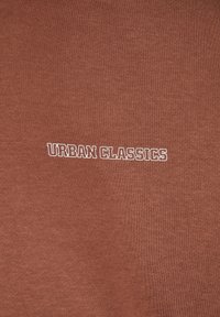 Tejido de algodón marrón con una superficie texturizada, con texto bordado en blanco "URBAN CLASSICS" centrado en el pecho.