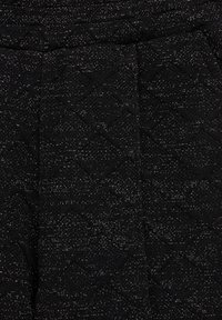 Zwarte textuurstof met een golvenpatroon en metallic accenten. Het materiaal lijkt geweven met een licht glanzende afwerking.