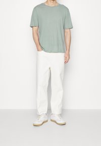 T-shirt en coton vert avec un col rond, associé à un pantalon blanc à coupe ample. Complété par des baskets blanches avec des semelles brunes.