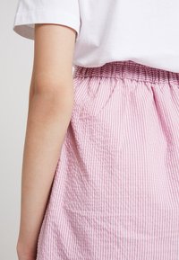 Jupe rayée rose et blanche avec une taille élastique, fabriquée en tissu texturé, partiellement visible à côté d'une manche de t-shirt blanc uni.