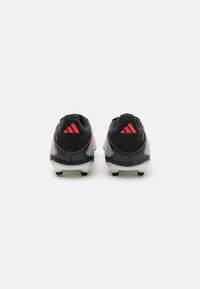 Zapatillas deportivas negras con un upper texturizado, detalles rojos y suelas blancas con clavos, que presentan un diseño aerodinámico y una marca distintiva.