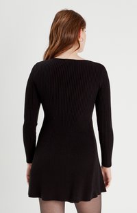 Czarna dzianinowa sukienka z długimi rękawami, z dopasowaną górą i rozkloszowanym dołem. Tekstura wydaje się lekko elastyczna i gładka.