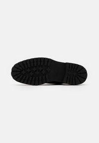 Semelle de chaussure en caoutchouc noir avec un motif de semelle robuste, présentant des rainures profondes et des sections surélevées pour une traction et une stabilité améliorées.