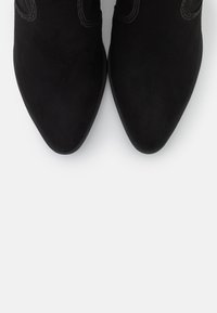 Czarne zamszowe botki sięgające kostki z podeszwą w szpic, ozdobione subtelnymi detalami szewnymi oraz gładką, elegancką powierzchnią.