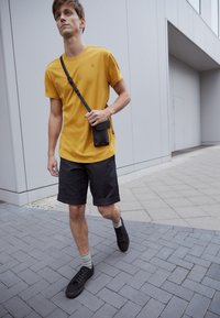 Yellow short-sleeve t-shirt, black knee-length shorts, black sneakers, and multicolored striped socks; crossbody black bag.
