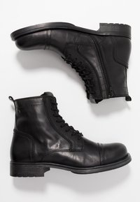 Botas de tobillo de cuero negro con acabado suave, cordones en la parte delantera, cremallera lateral y un tacón bajo con suela de goma texturizada.