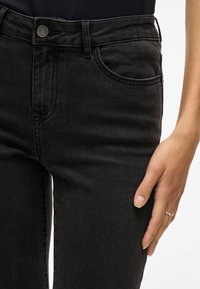 Jeans de mezclilla negros con un corte clásico, que cuentan con un bolsillo delantero, trabillas para cinturón y un cierre de botón metálico. Textura suave y costuras mínimas.