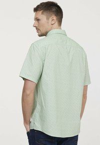 Hellgrünes kurzärmliges Hemd mit einem kleinen Blumenmuster, Button-Down-Kragen und seitlichen Schlitzen für mehr Bewegungsfreiheit.