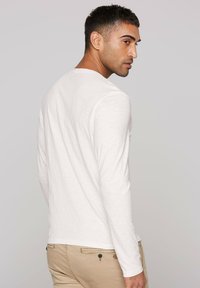 Langärmeliges weißes Hemd aus leichtem Stoff mit leichter Struktur, Rundhalsausschnitt, kombiniert mit hellen Hosen mit Taschen-Details.