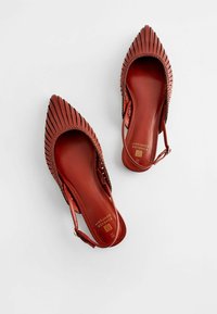 Escarpins slingback rouges avec des pointes pointues, présentant un design plissé et une texture lisse. À l'intérieur, une semelle rembourrée avec un détail de marque dorée.