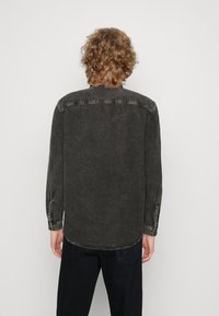 Mörkgrå denimskjorta med långa ärmar, knäppta manschetter och en rundad avslutning. Har blekningar och en enkel klassisk kragsdesign.