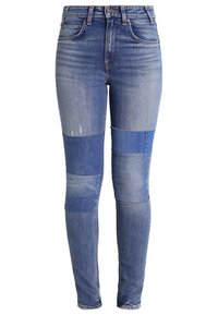 Vaqueros de mezclilla azul descoloridos con un diseño de patchwork en diferentes tonos de azul, de tiro alto y estilo ajustado.