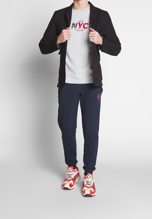 Sort blazer over en grå t-shirt med rød og blå NYC tryk, parret med marineblå joggers og flerfarvede mønstrede sneakers.
