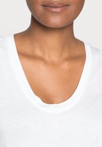 T-shirt bianca in cotone con scollatura ampia e maniche corte, caratterizzata da una texture liscia e una vestibilità comoda.