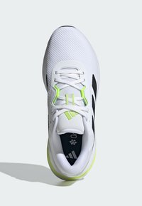 Zapatilla deportiva blanca con parte superior de malla, acentos negros y detalles en verde fluorescente. Cuenta con un collar acolchado y sistema de lazado.