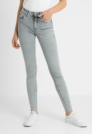 Vaqueros ajustados de mezclilla en gris claro, diseño de cintura alta, cinco bolsillos, costuras en contraste, combinados con zapatillas blancas.