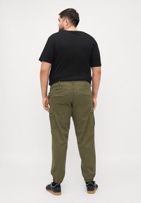 Olijfgroene cargobroek met elastische boorden, meerdere zakken en een regular fit, gecombineerd met een zwarte T-shirt met korte mouwen.