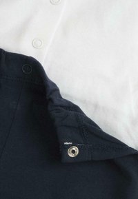 Tissu en coton blanc et marine superposé, avec des boutons-pression en métal argenté. Texture douce avec des coutures propres et sans motifs visibles.