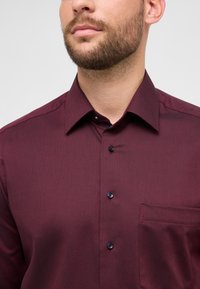 Bordeaux rode overhemd met knopen, een gestructureerd patroon, een spitse kraag, zwarte knopen en een borstzak, gemaakt van gladde stof met een getailleerde pasvorm.
