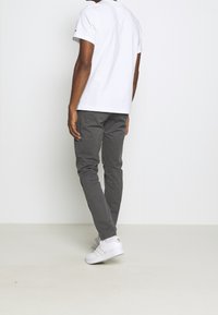 Šedé slim-fit kalhoty v kombinaci s bílým tričkem a bílými teniskami, s jednoduchým designem a čistými liniemi. Žádné viditelné vzory ani akcenty.