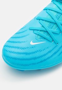 Turbánkék focicipő, texturált szintetikus felsőrésszel, hullámos mintázattal és fehér Nike emblémával. A fűzők szintén turbánkék színűek.