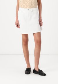 Jupe mini en denim blanc avec une légère évasement, dotée d'un design à cinq poches et d'une fermeture à bouton à l'avant. Texture lisse et style décontracté.