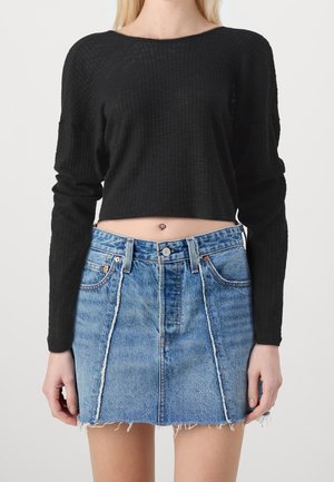 Haut court à manches longues noir à côtes, associé à une jupe en denim taille haute bleu clair avec un ourlet effiloché et des détails de couture contrastants.