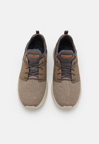 Zapatillas marrones de malla con parte superior texturizada, detalles en gris y plantilla con patrón. Tienen punteras redondeadas y cordones negros.