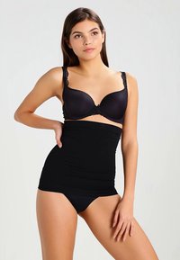 Woman wearing black high-waist shapewear, black bra with lace straps, and black underwear, posing with one hand on hip against plain background.