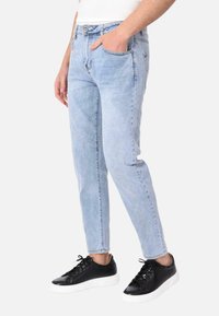 Jeans in denim azzurro chiaro con una vestibilità slim, caratterizzati da un classico design a cinque tasche e una chiusura con bottone. Indossati con sneakers nere.