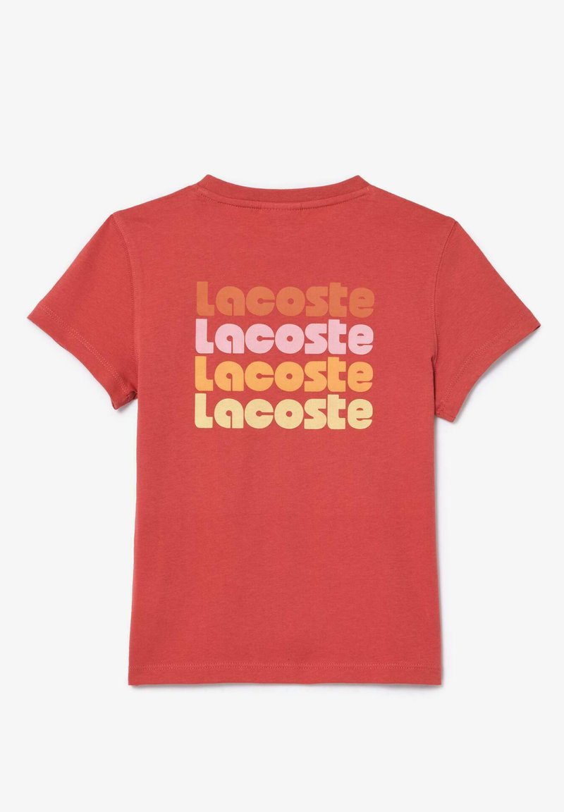 Rotes Baumwoll-T-Shirt mit wiederholtem "Lacoste"-Text in Retrofarben: Orange, Pink und Gelb, prominent auf der Rückseite dargestellt.