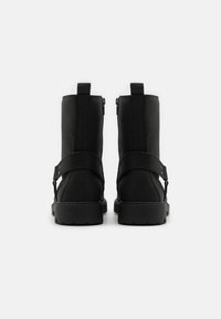 Botas negras de tobillo con un upper texturizado, doble cremallera y una correa en la parte media. Suela de goma resistente con diseño plano.