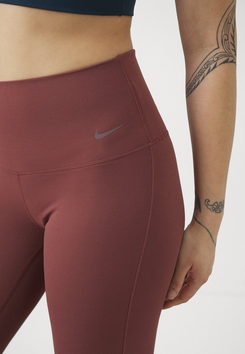 Bordeaux yogabroek met hoge taille, een gladde textuur, subtiele rek, en een klein grijs Nike-logo vlakbij de tailleband.