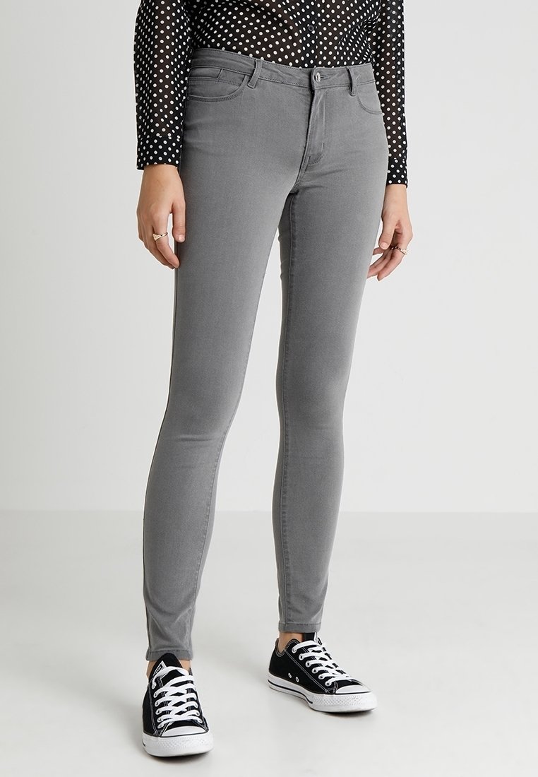 Personne portant un jean gris slim, un haut à manches longues à pois noirs et blancs, et des baskets basses noires avec des lacets blancs.