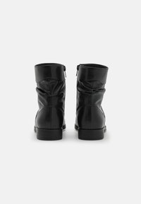 Bottes au cheville en cuir noir avec un design froissé, présentant une texture lisse et un talon bloc bas, accentuées par des fermetures éclair à l'arrière.