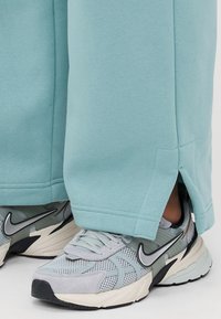 Lyseblå joggebukser med sidespalter i hemmen, kombinert med grå og hvite Nike-sneakers med mesh- og semsket detalj.