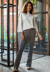 Lichtgrijze, geweven trui met driekwart mouwen, gecombineerd met gestreepte zwart-witte broeken. Zwarte schoenen met crèmekleurige zolen maken de outfit compleet.