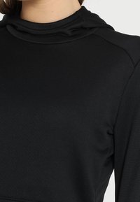Felpa con cappuccio nera indossata da una persona, che mostra la parte superiore del torso e il collo con un dettaglio di tessuto arricciato.