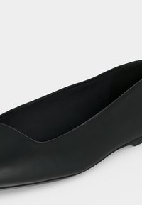 Chaussure plate noire avec un bout arrondi et une texture lisse, conçue pour un usage décontracté ou formel.