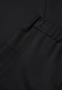 Zwarte broek met een elastische tailleband, gladde textuur en een zijzak met minimale stikseldetails.