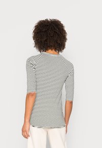 Camiseta de manga larga a rayas en negro y blanco, con un corte ajustado y mangas raglán, fabricada con un tejido de tacto medio-suave y con escote redondeado.