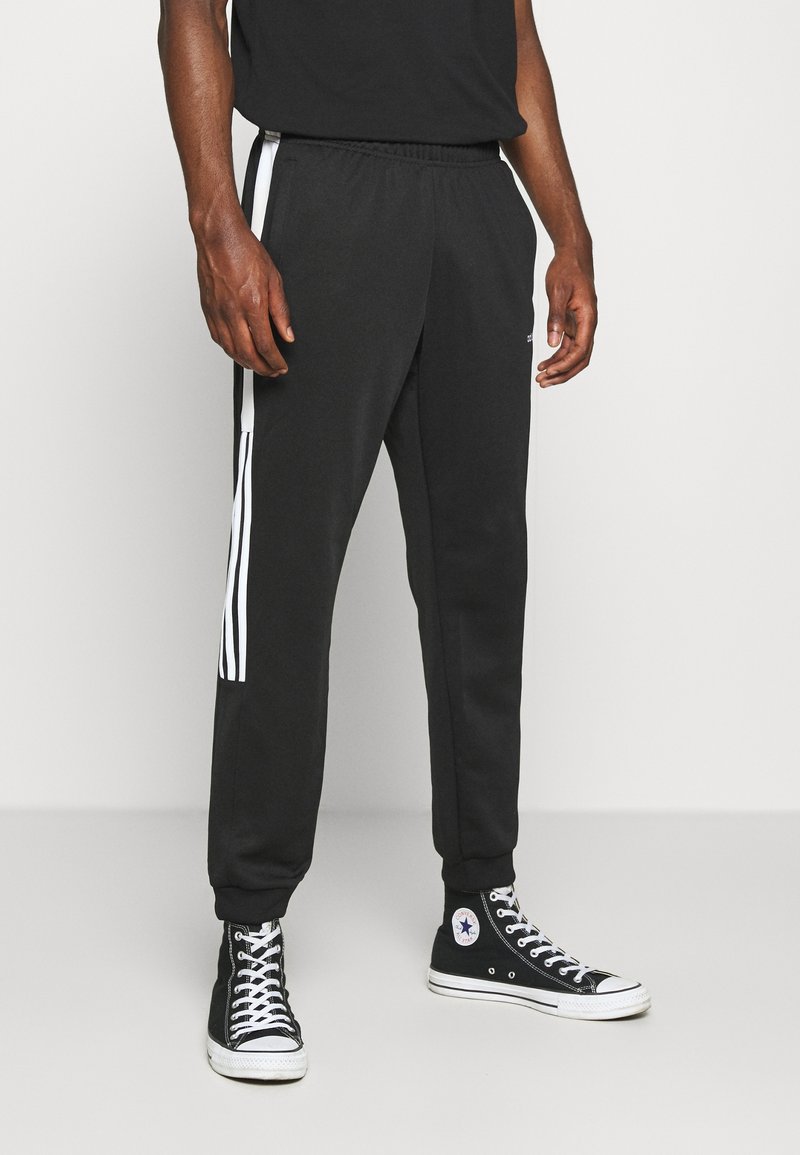 Black athletic pants with white stripes down the sides, elastic waistband, and cuffed ankles, paired with black high-top sneakers.