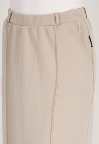 Beige rechte pijpenbroeken van zachte stof met een elastische tailleband, voorzien van zijzakken en een subtiele verticale stiknaad.