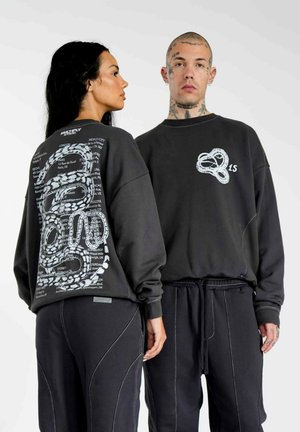 Grå oversized sweatshirts med unikke grafiske tryk på ryggen og forsiden, parret med sorte drawstring-bukser med kontrastsyninger.