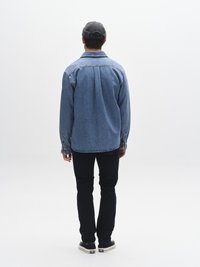 Helehallinine teksariidest särk pikkade varrukate ja nööpidega mansettidega, kombineeritud tumedate teksade ja mustade tossudega, vaadatuna tagantpoolt.