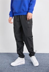 Svarta cargobyxor med en texturerad yta, sidofickor och en subtil Nike-logotyp som accent. Kombineras med vita Nike-sneakers.