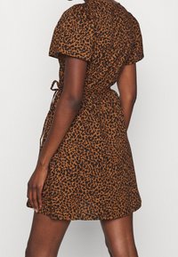 Robe imprimé léopard en nuances de marron et noir avec manches courtes, taille cintrée et détail noué à l'arrière, confectionnée dans un tissu léger.