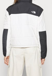 Pikowana kurtka w białym i czarnym kolorze. Posiada wysoki kołnierz, poziome bloki kolorów oraz logo North Face na plecach. Lekki materiał.