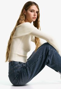 Ribbed off-shoulder white sweater paired with high-waisted blue denim jeans, featuring a relaxed fit and minimal stitching details.