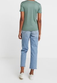 Grön t-shirt med kort ärm, kombinerad med ljusblå jeans med rå kant. Modellen bär vita Reebok-sneakers. Avslappnad och bekväm passform.